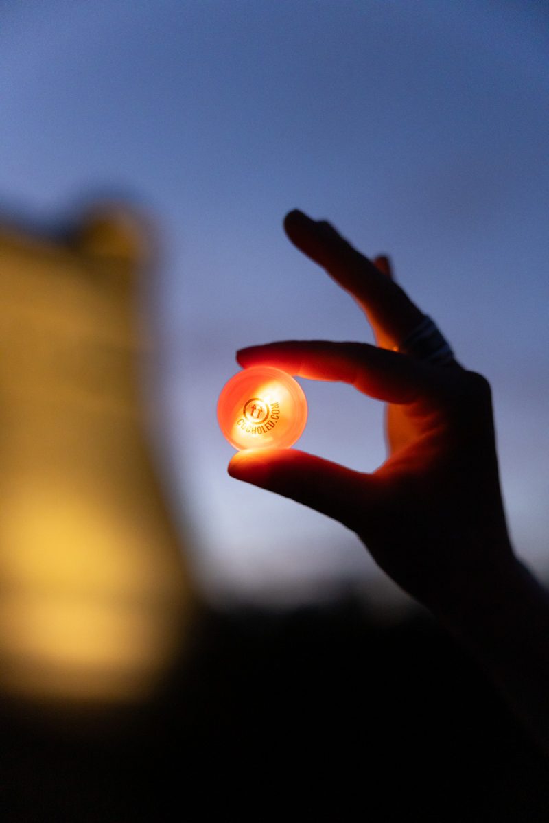 Cochonnet lumineux Cocholed orange tenu à la main, illuminé lors d'une partie de pétanque en soirée, avec une lumière douce en arrière-plan